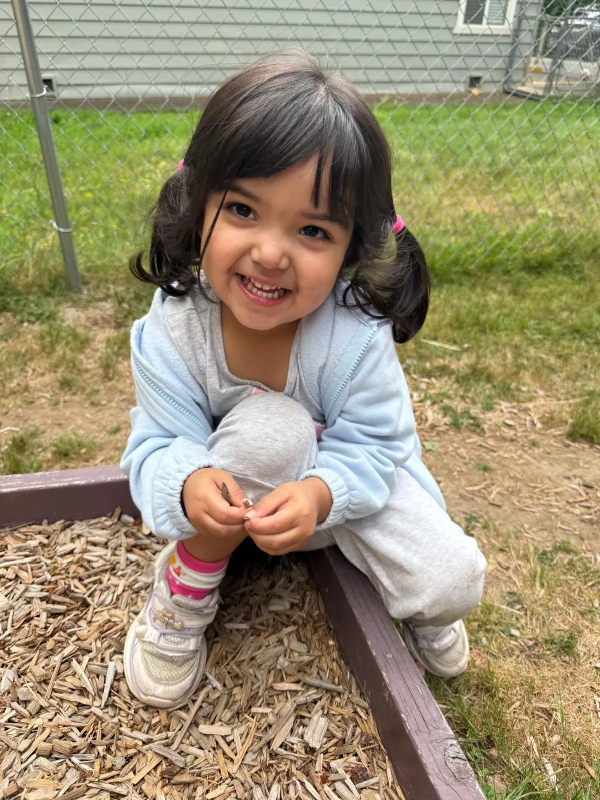A giggling girl crouching by the playground wood chips