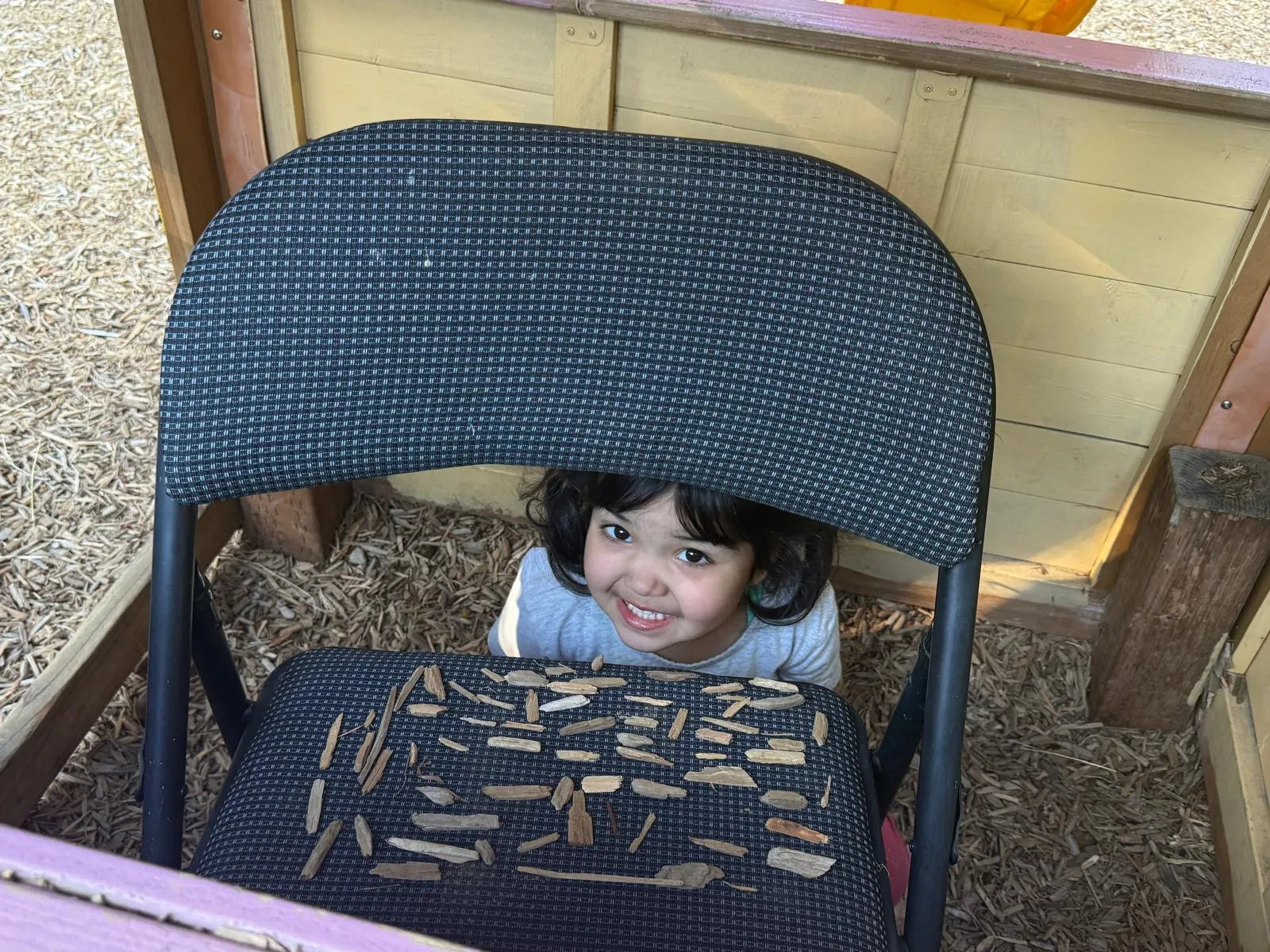 A girl peeking over her wood-chip pattern on a chair