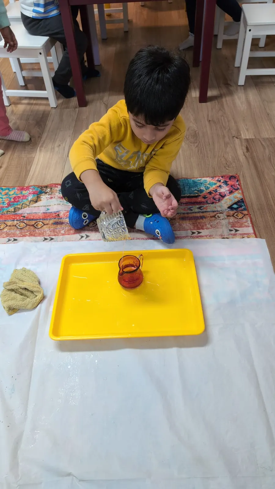 A child practising pouring on a yellow work tray