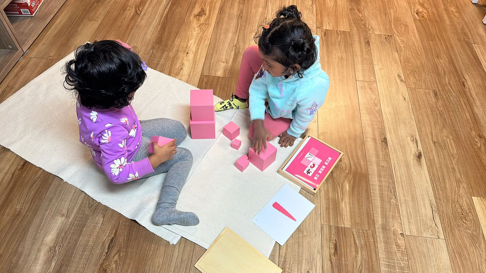 Two children building with the pink tower cubes