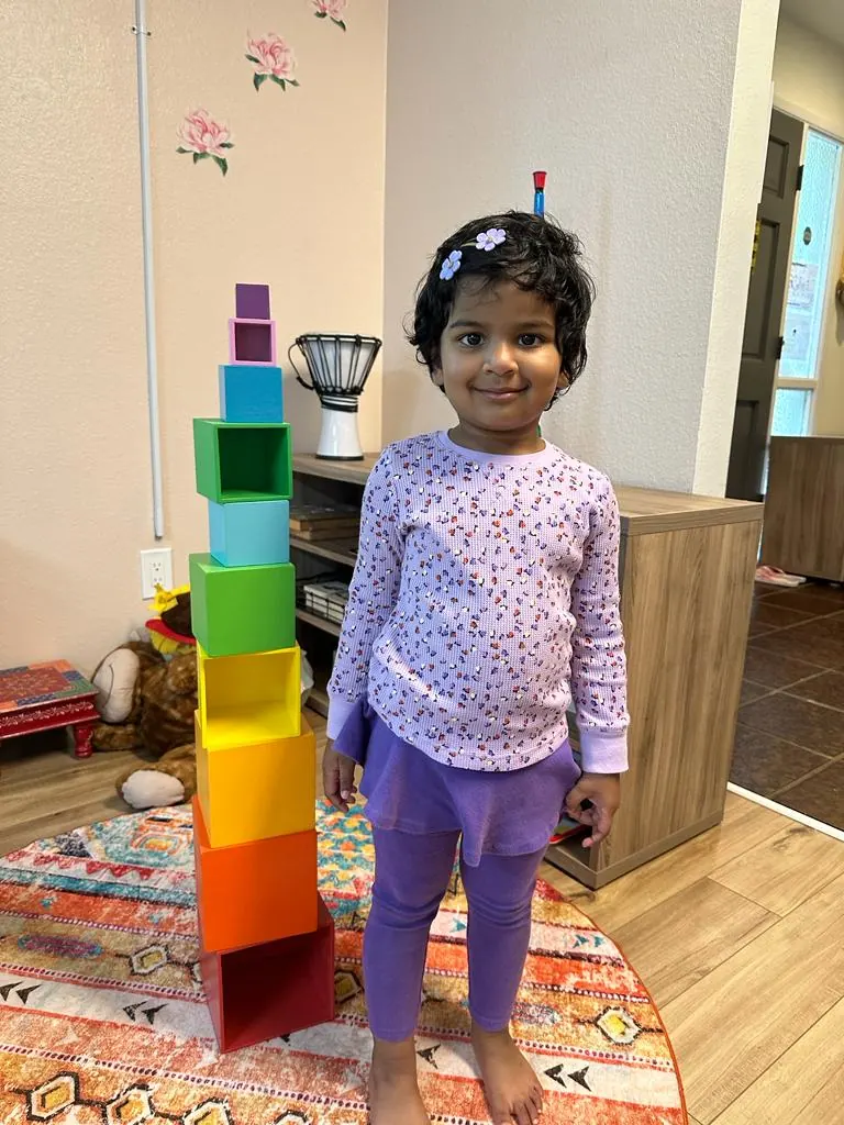 A smiling girl beside a rainbow stacking tower she built