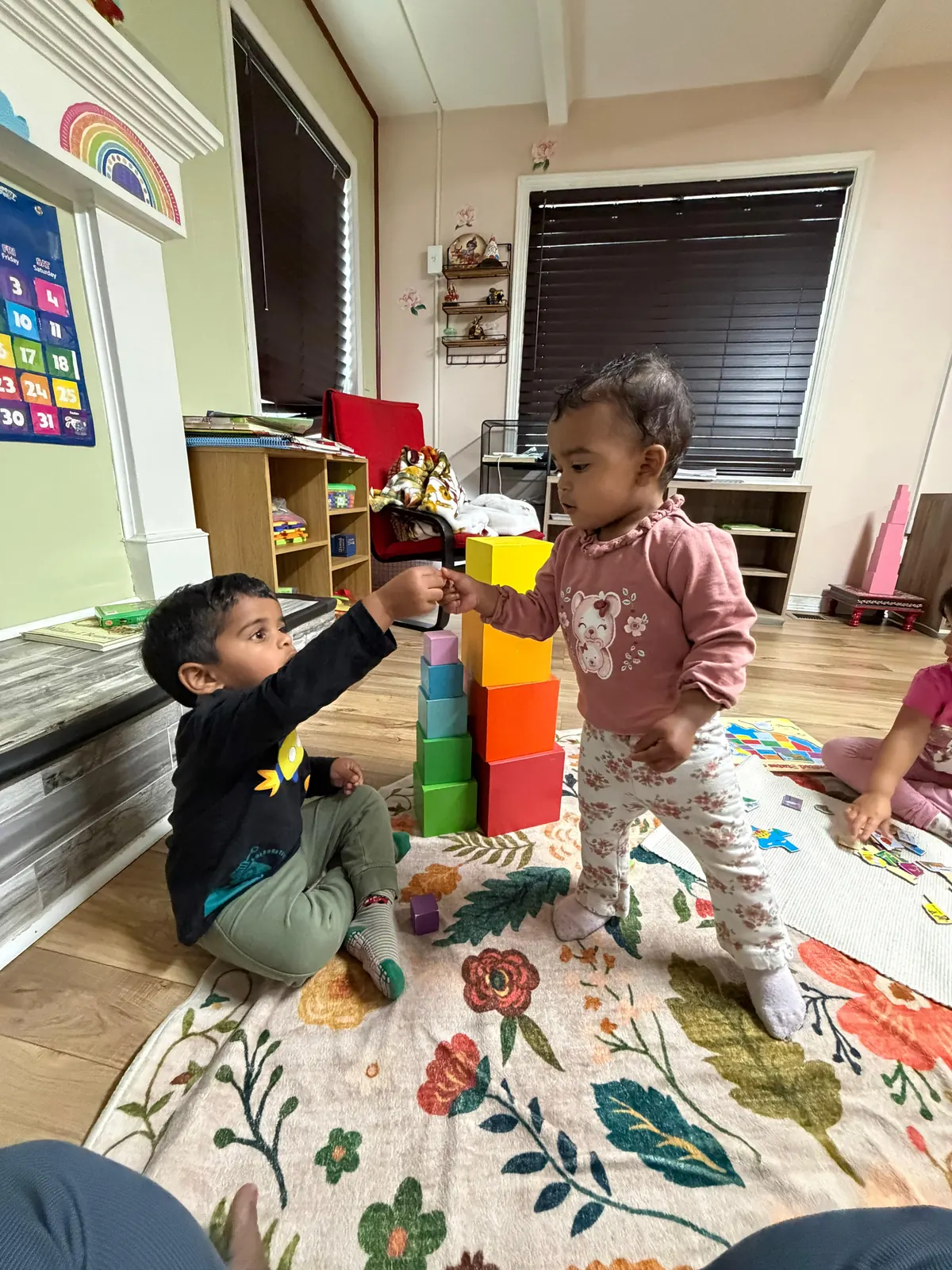 Two toddlers sharing blocks while building a rainbow tower
