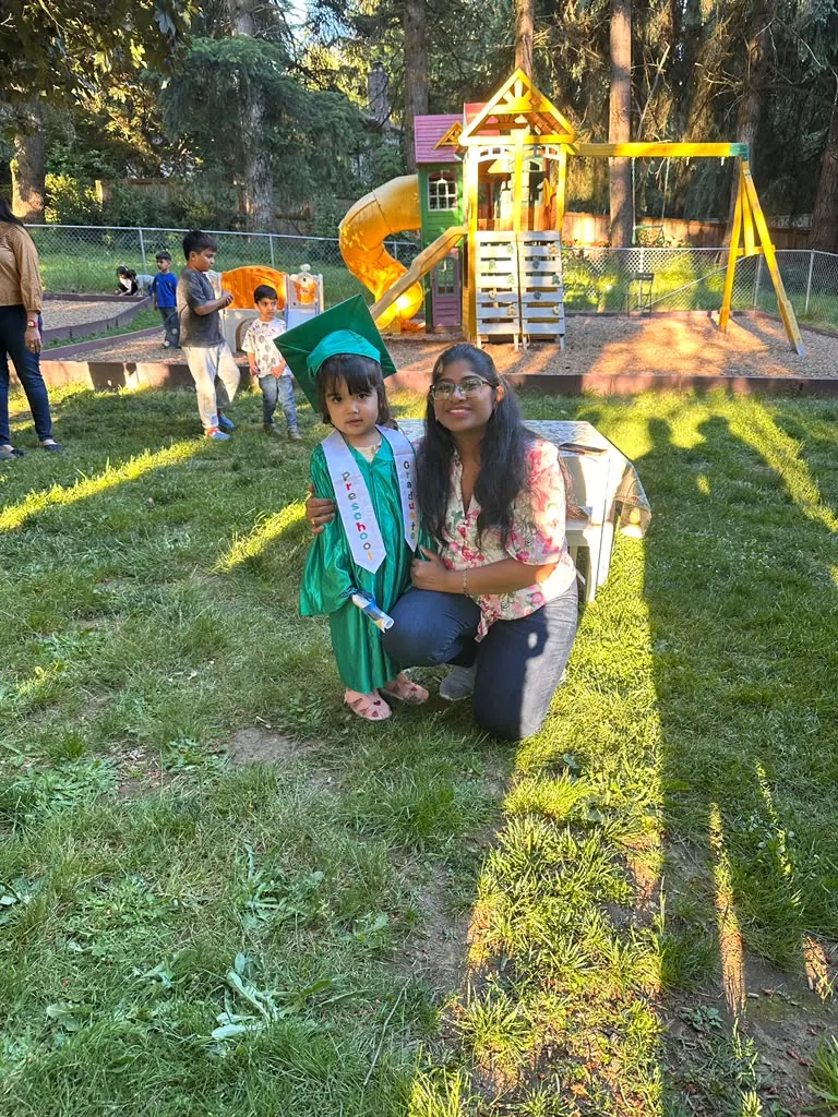 A graduate and teacher kneeling on the grass at golden hour