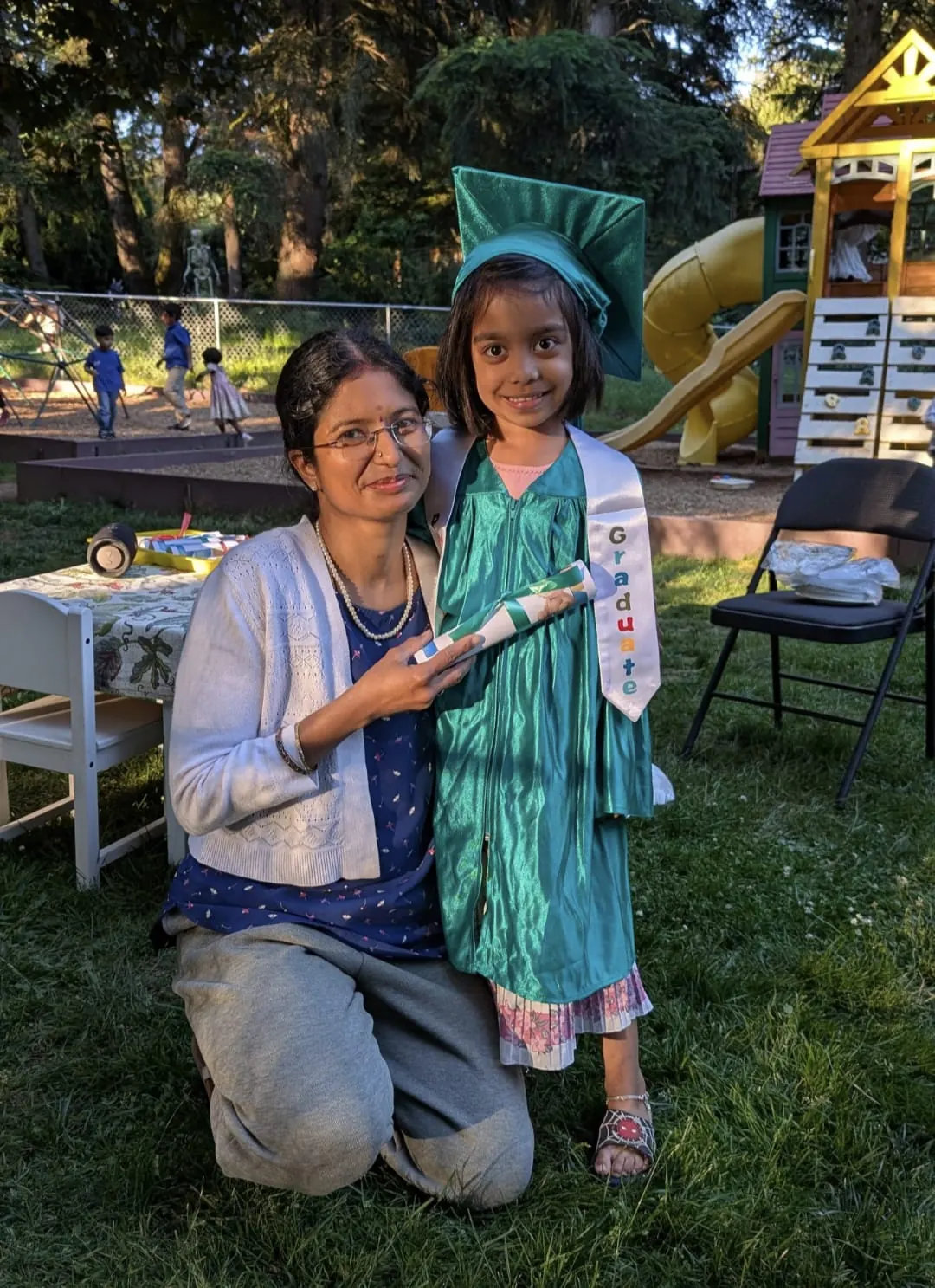 A teacher kneeling beside a graduate holding her diploma