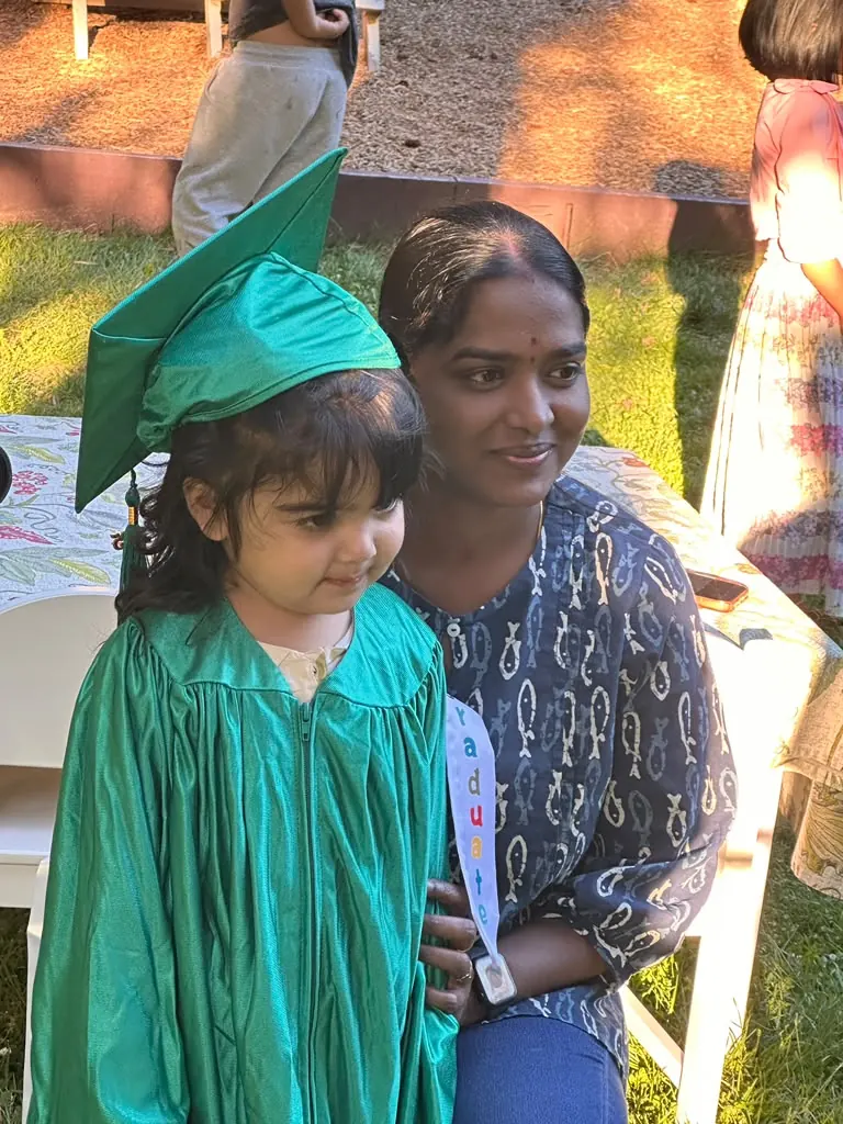 A little graduate in her cap beside her teacher