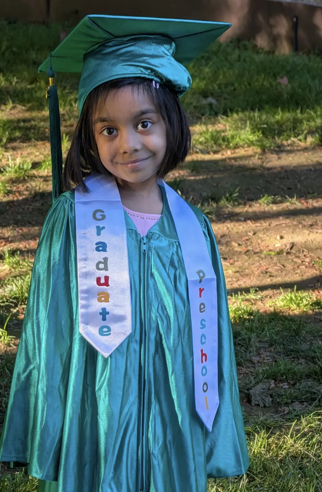 A proud preschool graduate in a green gown and graduate sash